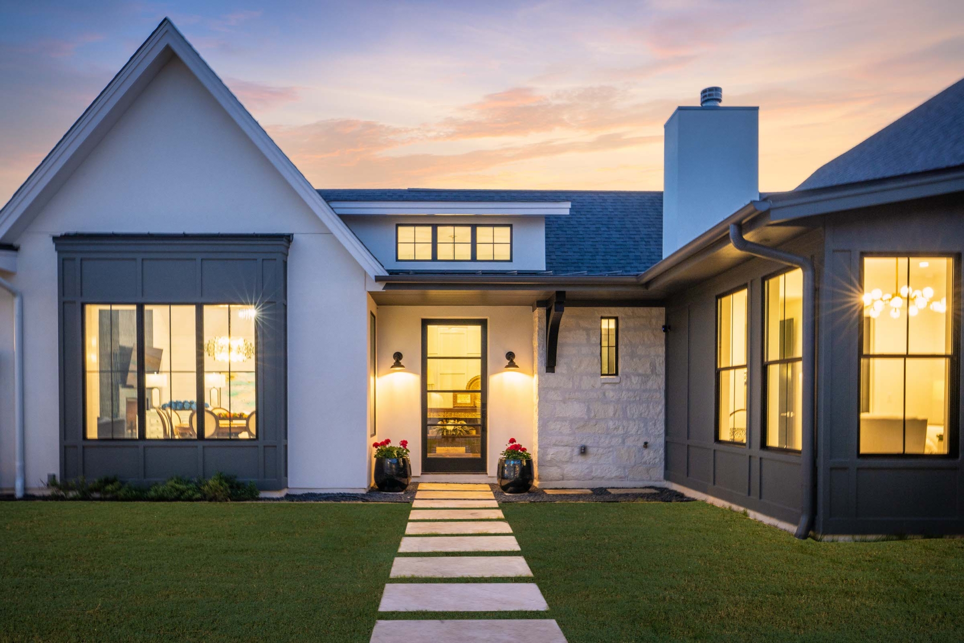Custom home in the Austin Texas region with large windows, white siding, and well landscaped yard and entryway